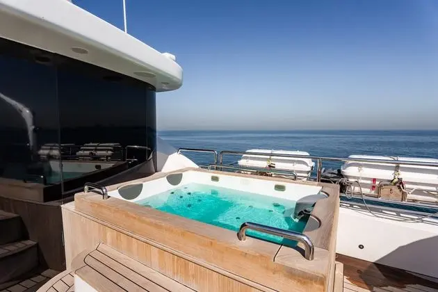 Deck jacuzzi with wooden surround and bubbling turquoise water overlooking the open sea