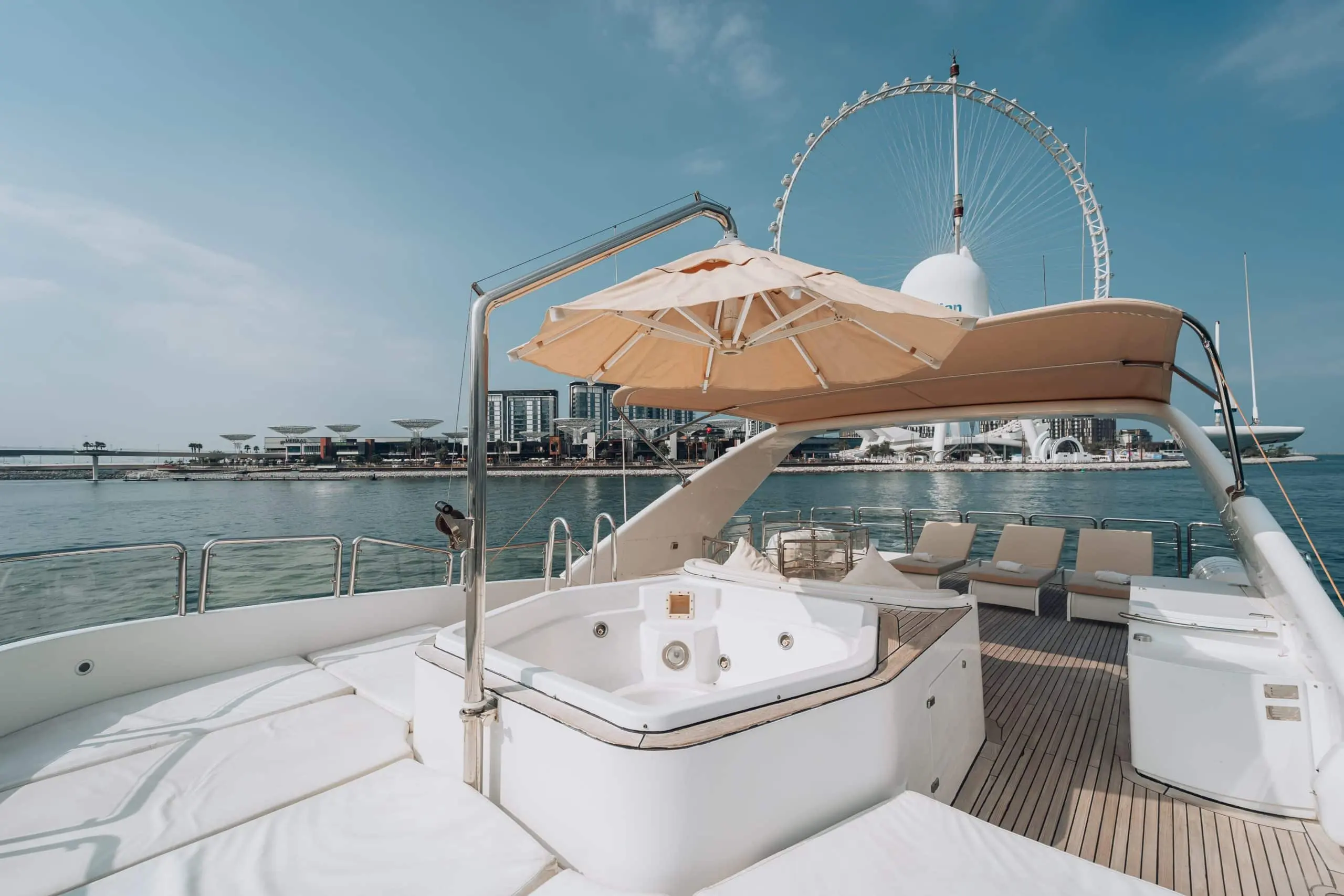 Luxury yacht deck with jacuzzi and sun loungers overlooking the waterfront and Ain Dubai in Dubai on a clear sunny day.