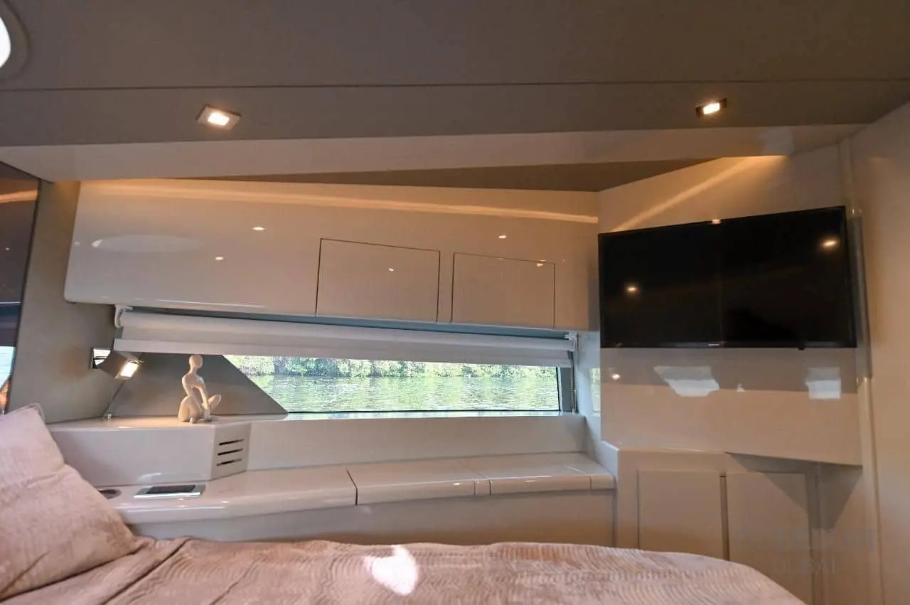 Novia 55 cabin with gloss white lockers, a vanity shelf, wall-mounted TV and a blind-shaded hull window