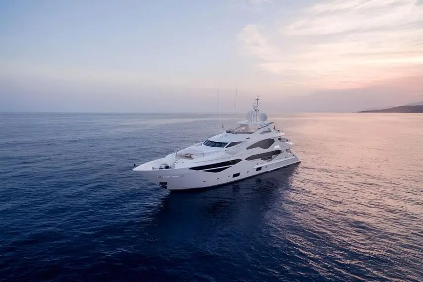 White superyacht cruising alone across calm open water under a soft pink dusk sky