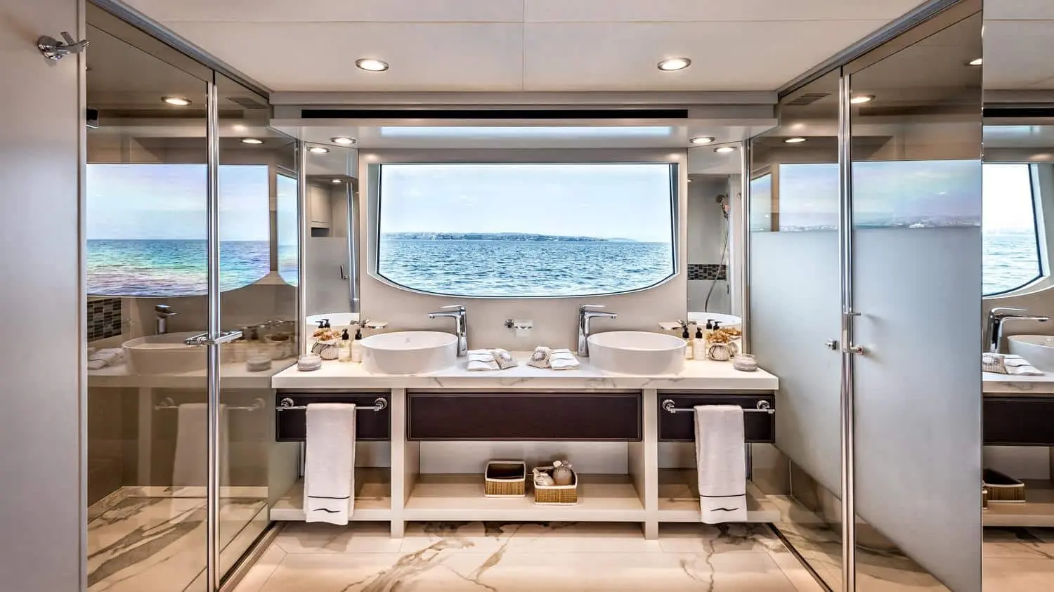 Luxury yacht bathroom interior with double sinks, marble flooring, glass shower, and large window overlooking the ocean.