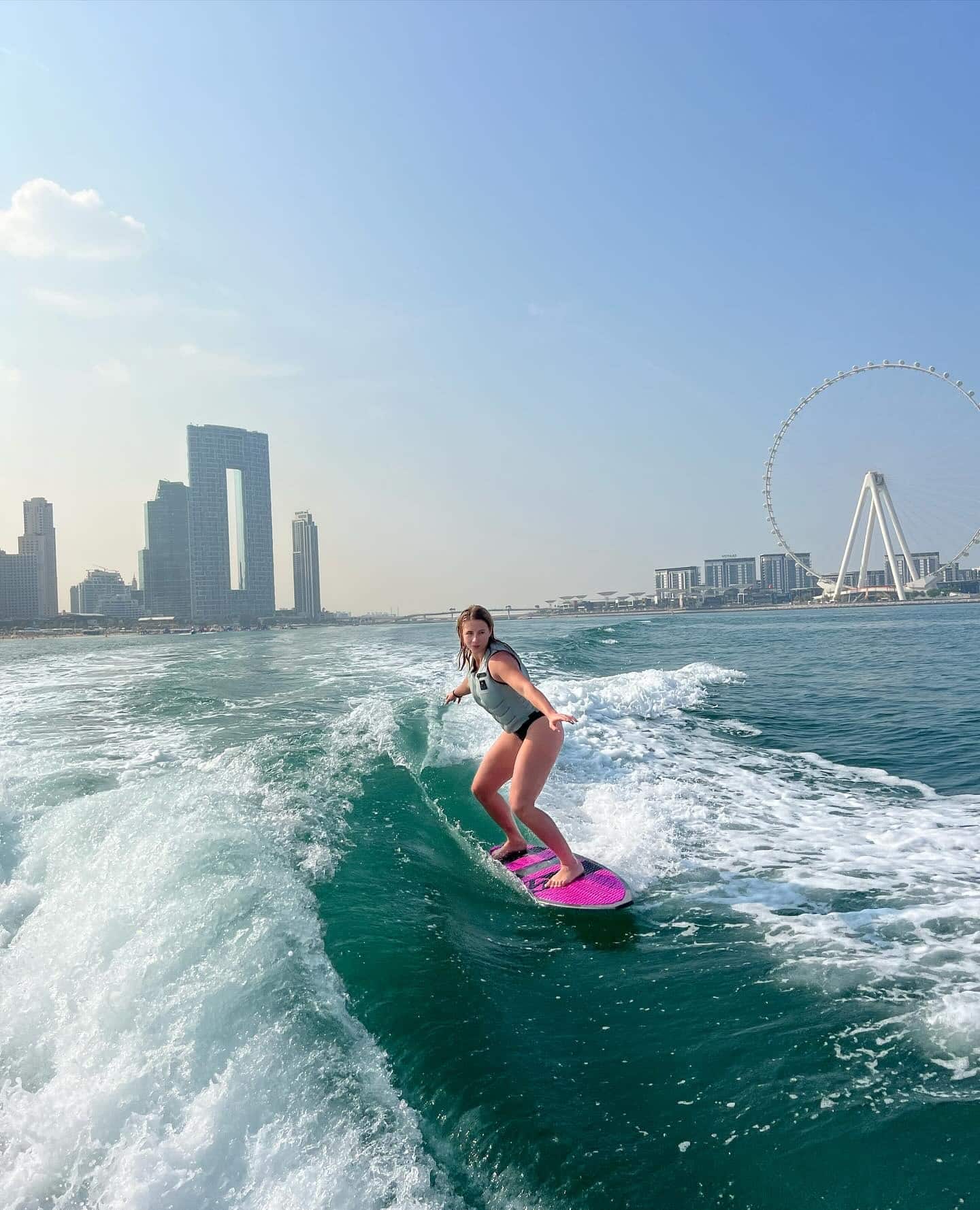 Wakesurfer riding the boat's wave with Ain Dubai and the coastline in the background