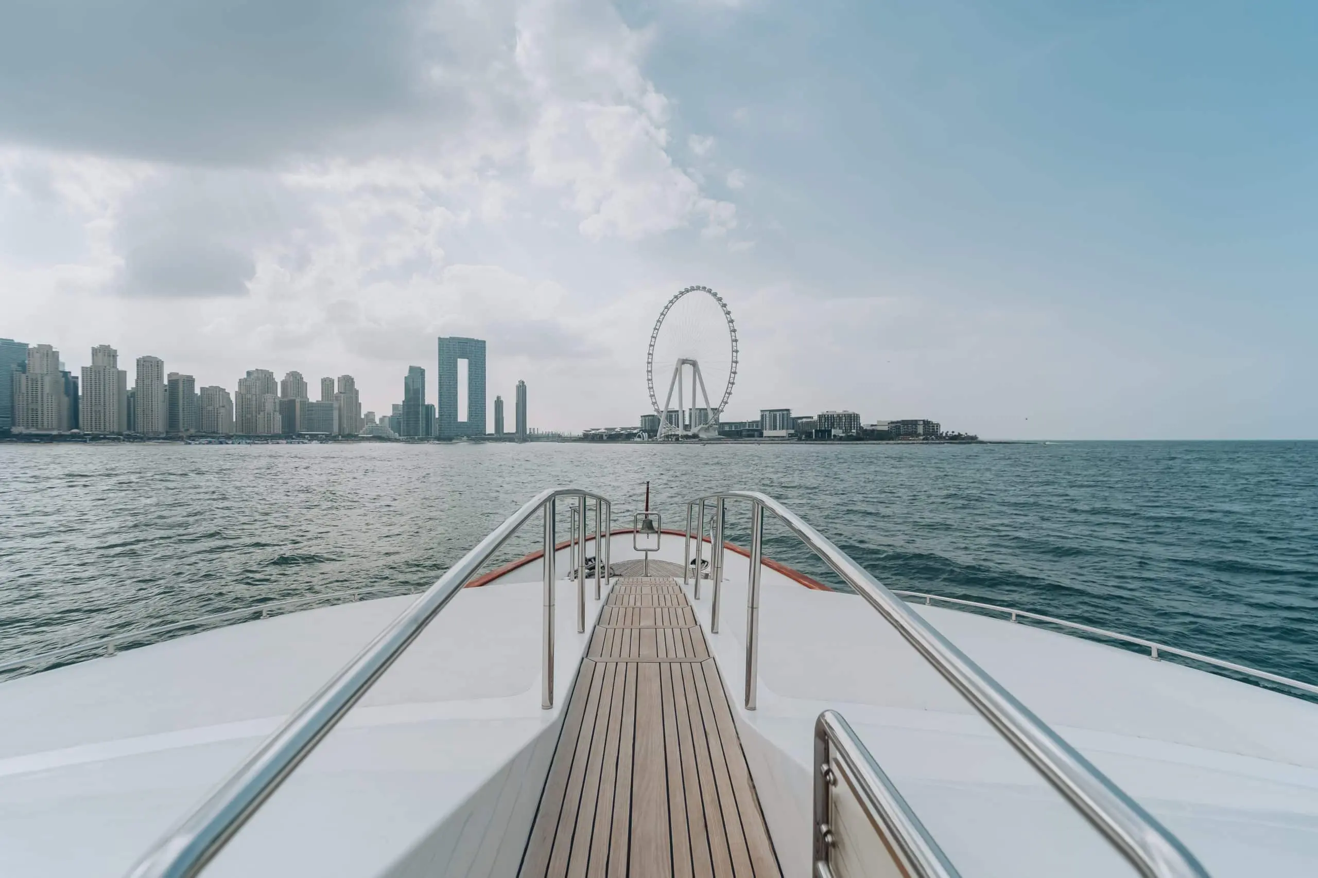 Yacht heading toward city skyline and Ferris wheel.