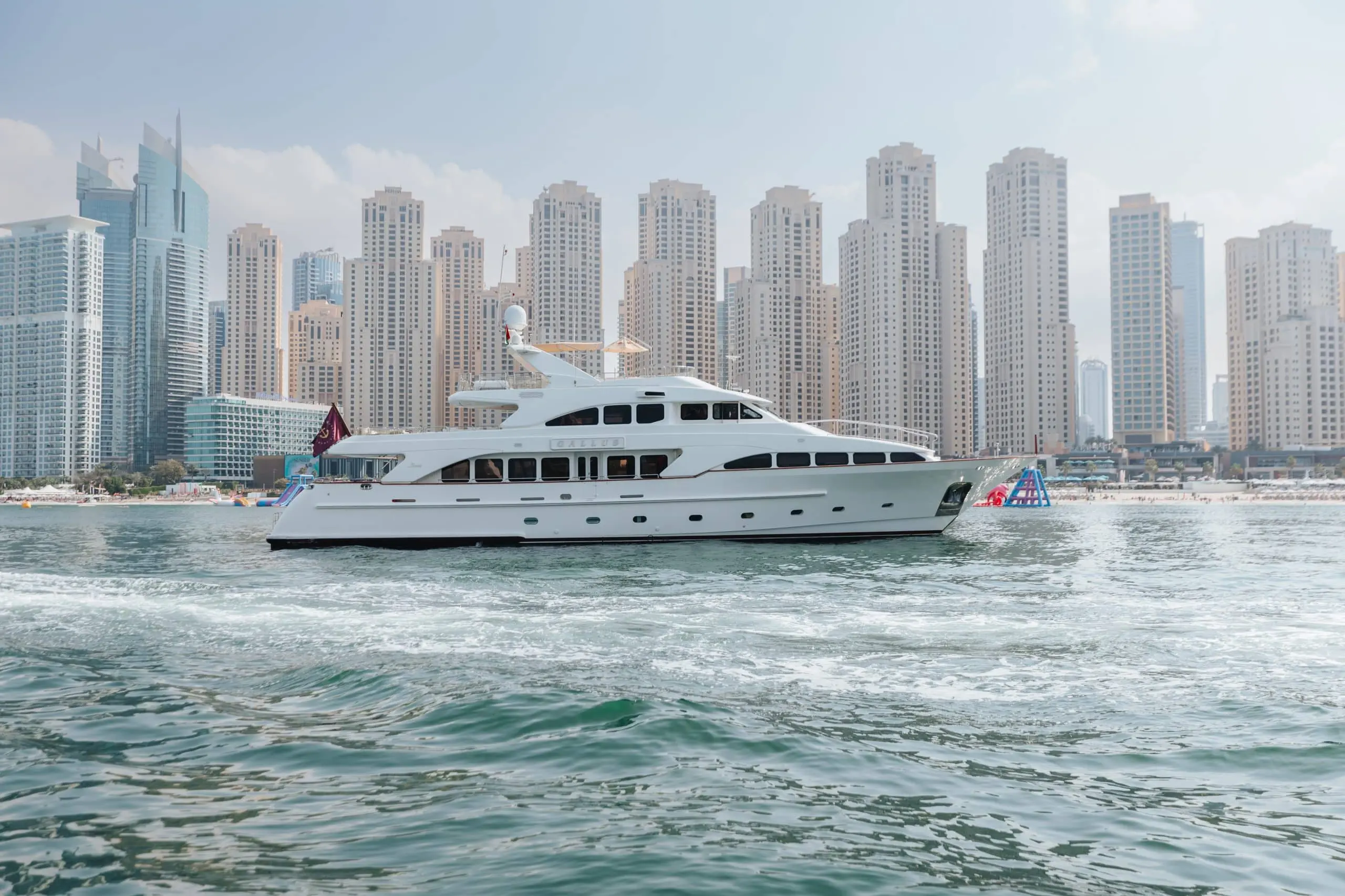 Luxury yacht cruising along the coastline of Dubai Marina, Dubai with high-rise skyline in the background.