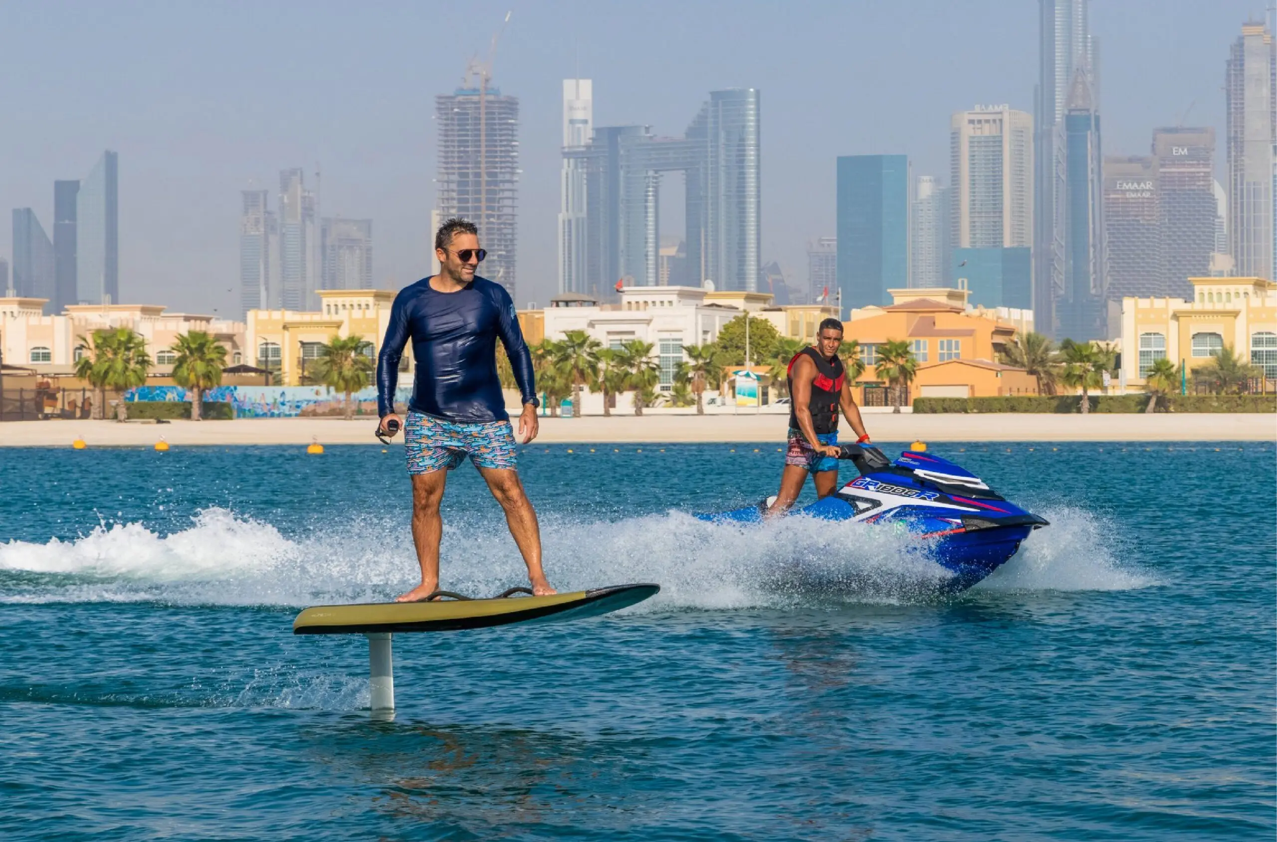 Rider on an electric hydrofoil board lifted above the water with a jet ski and the Dubai skyline behind