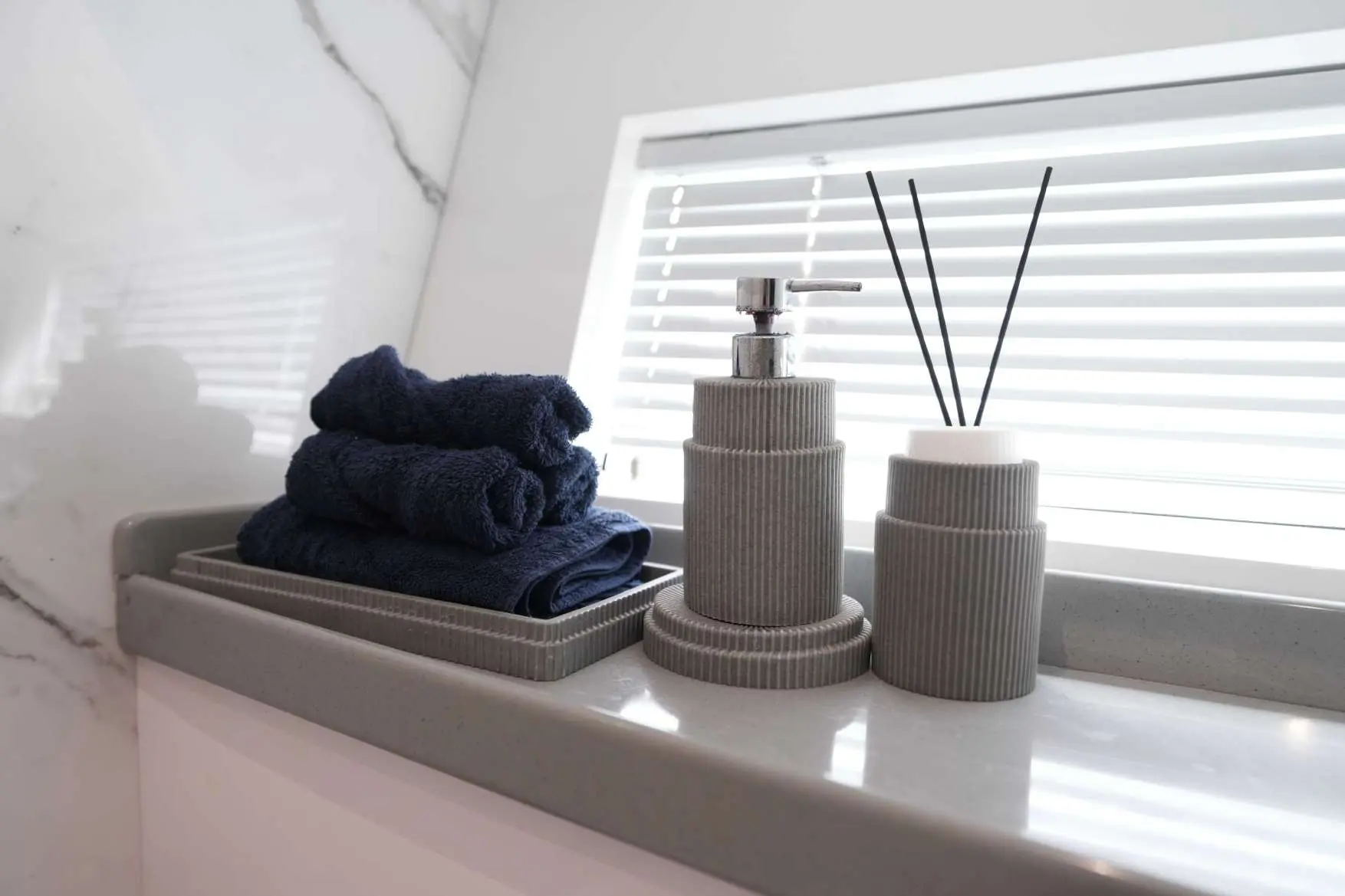 Luxury bathroom interior on Belle 75 yacht featuring folded navy towels, modern soap dispenser, and reed diffuser on marble countertop.