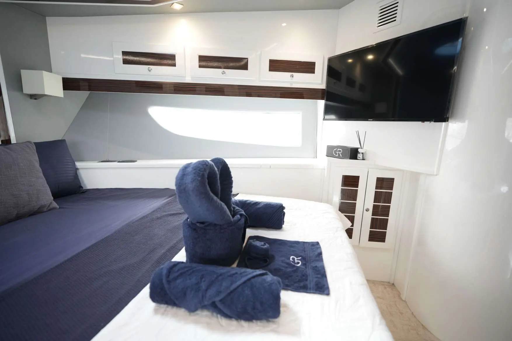 Belle 75 yacht master cabin with navy towels and wall-mounted TV.
