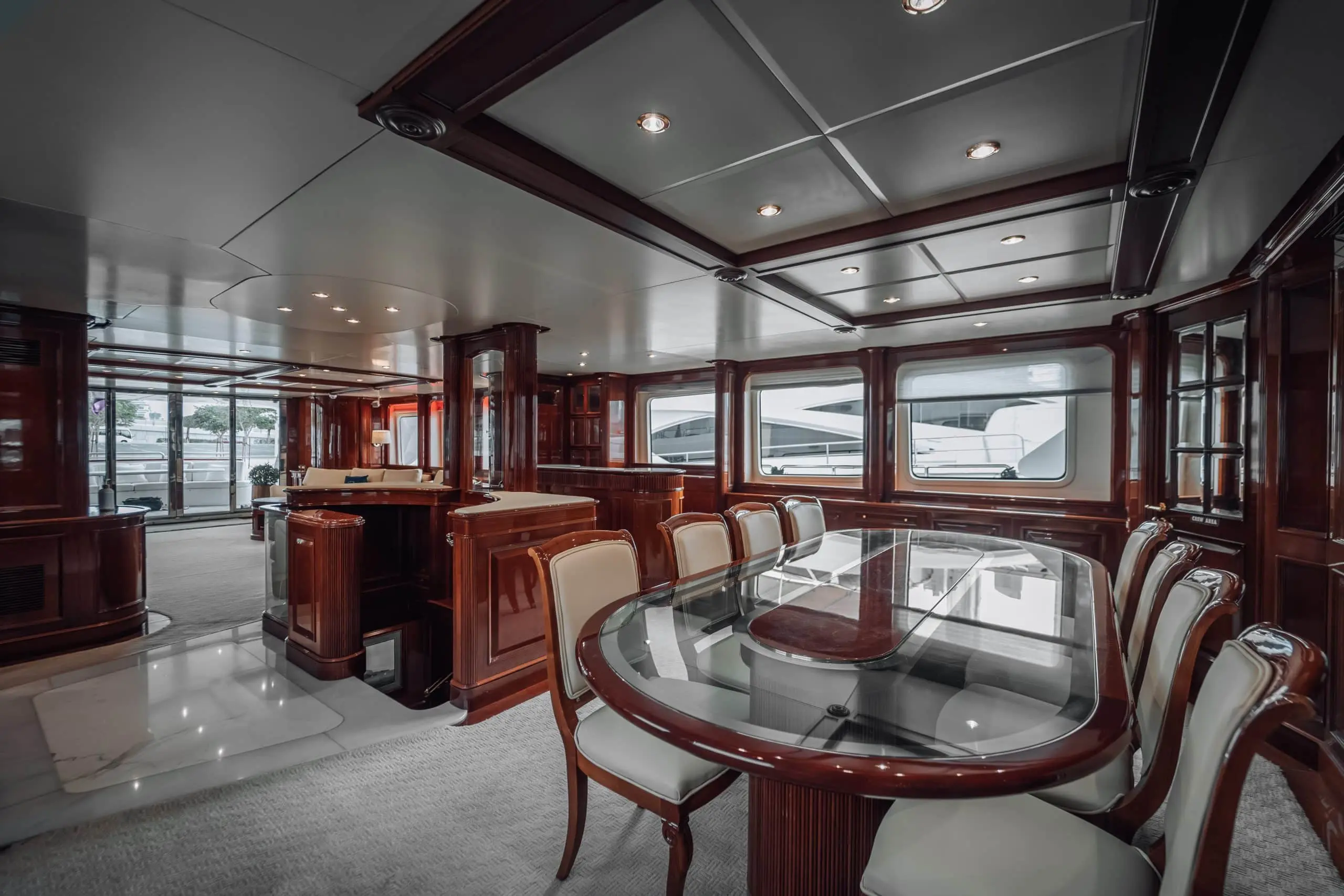 Luxury yacht interior with glass dining table and polished wood finishes.
