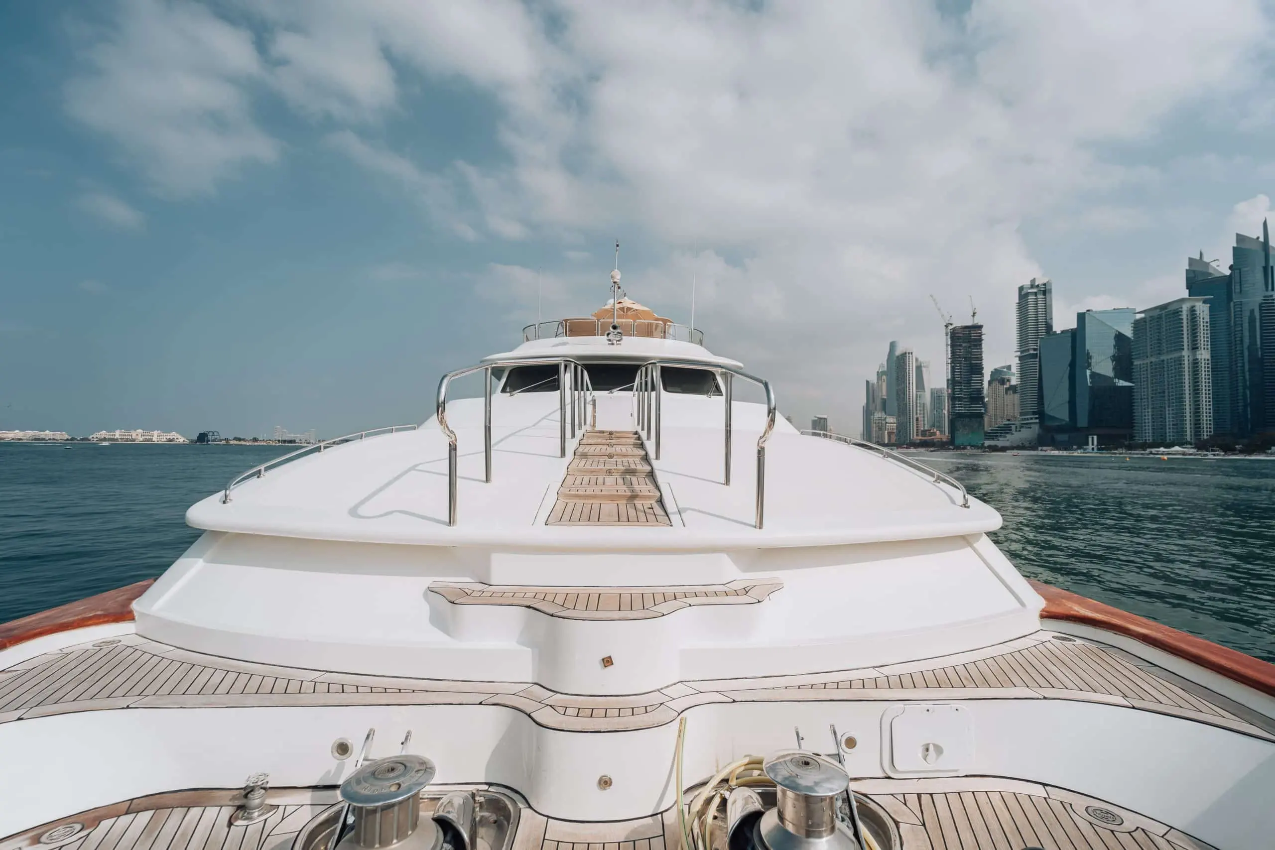Front deck of a luxury yacht facing a modern city skyline across calm water.