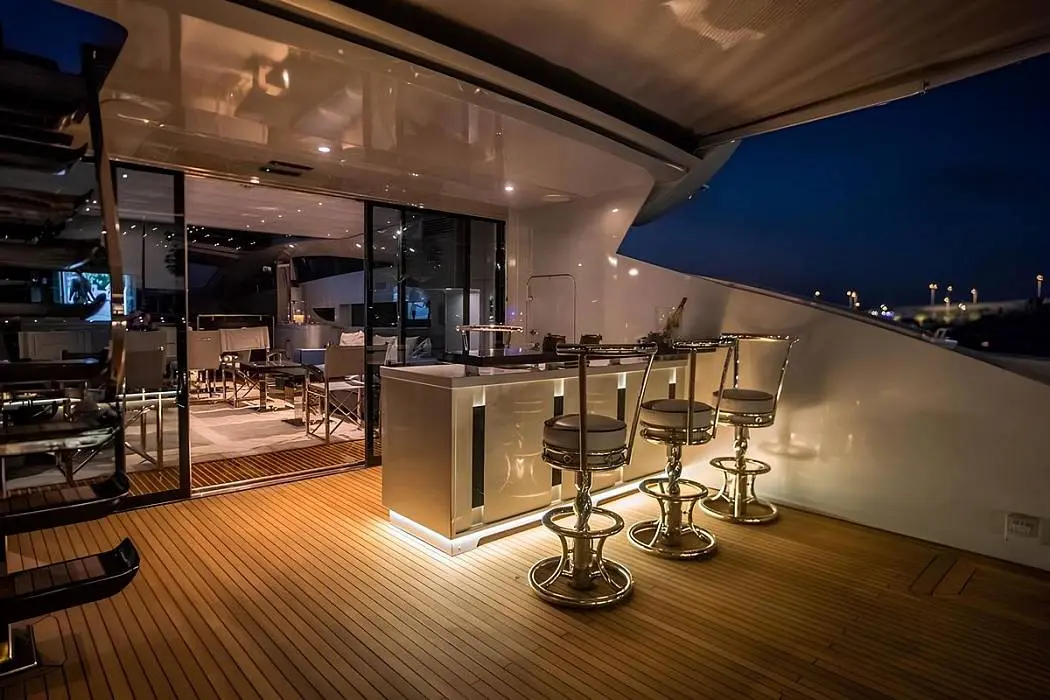 Baglietto 110 yacht outdoor deck bar with high stools, wooden flooring, and ambient evening lighting