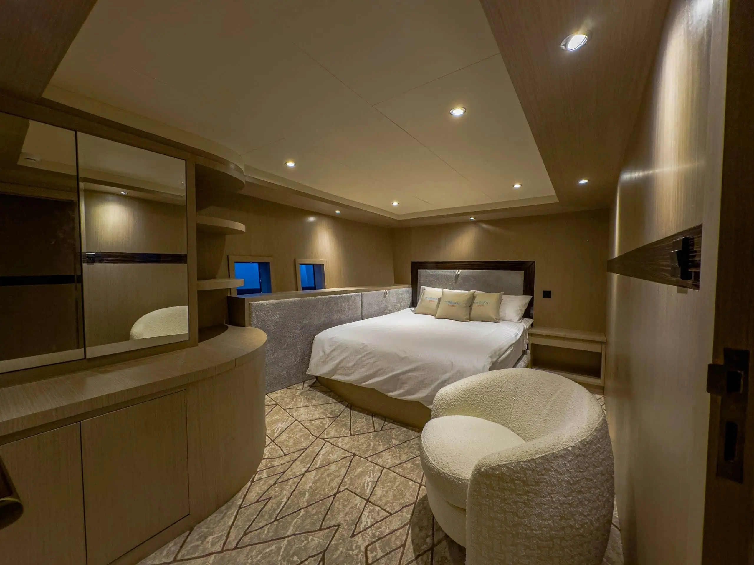 Warm-toned yacht suite with bed, seating area, and built-in storage shelves
