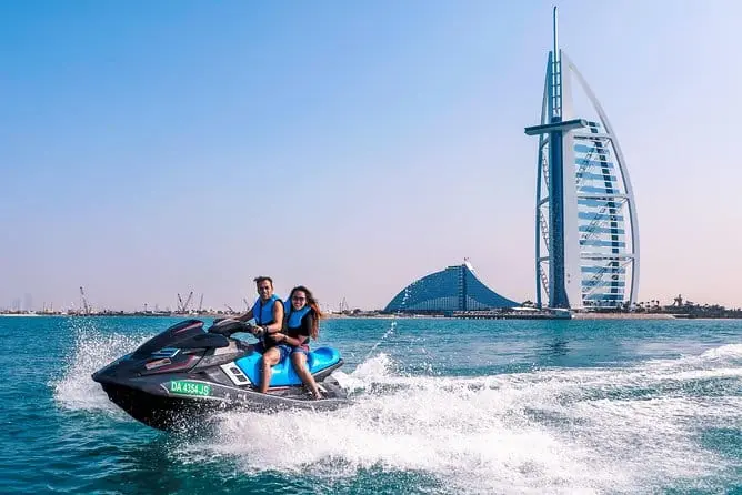 Two riders in life jackets on a jet ski speeding past the Burj Al Arab in Dubai