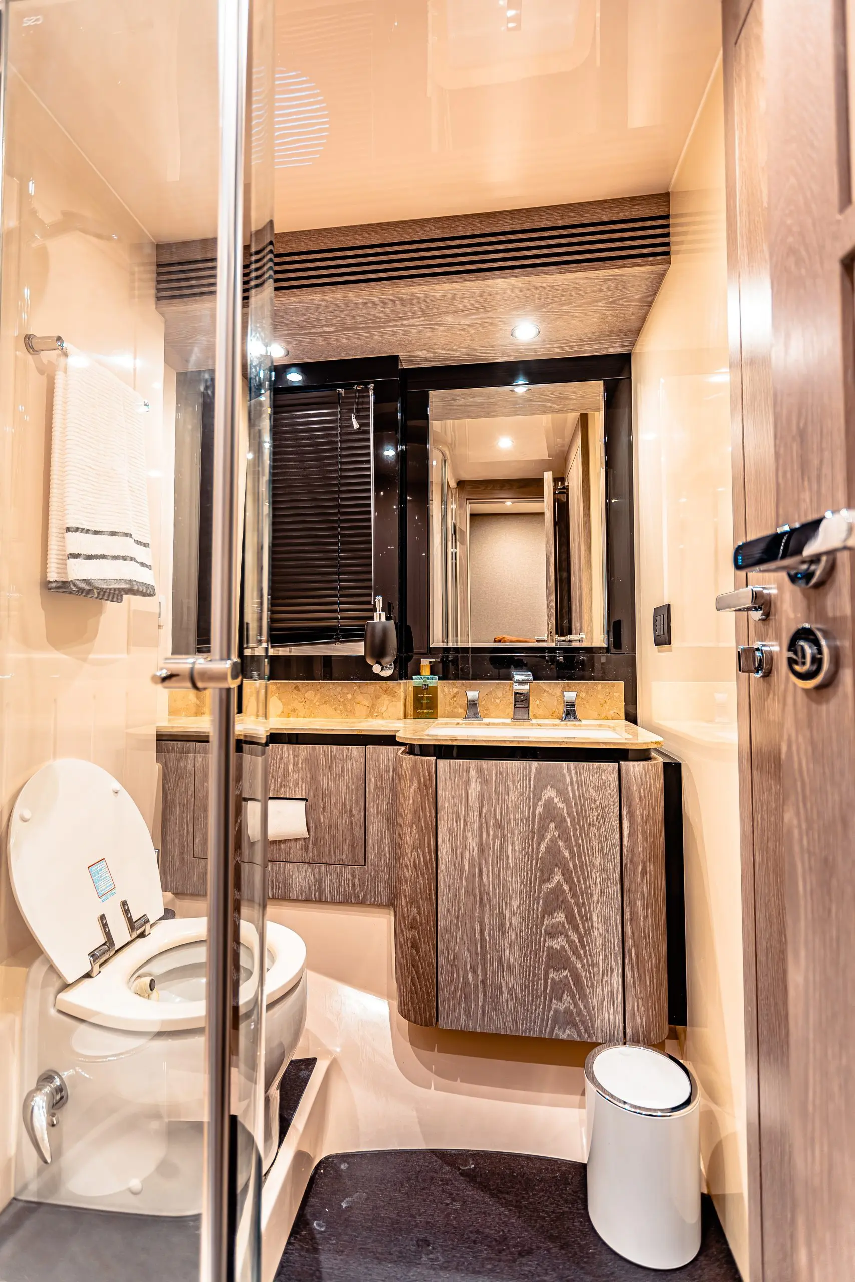 Yacht guest bathroom with glass shower, dark wood vanity, mirror and folded white towels