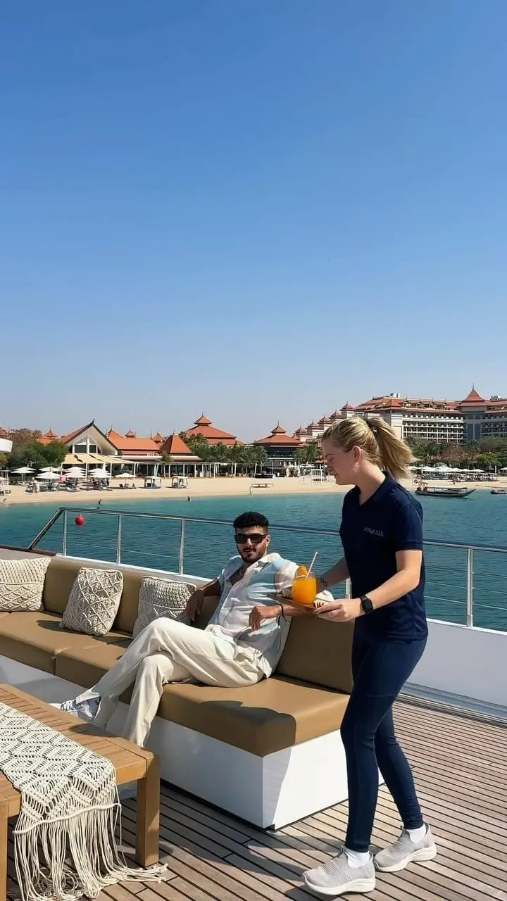 Crew member serving fresh juice to a guest lounging on the aft deck sofa of the Finesse yacht