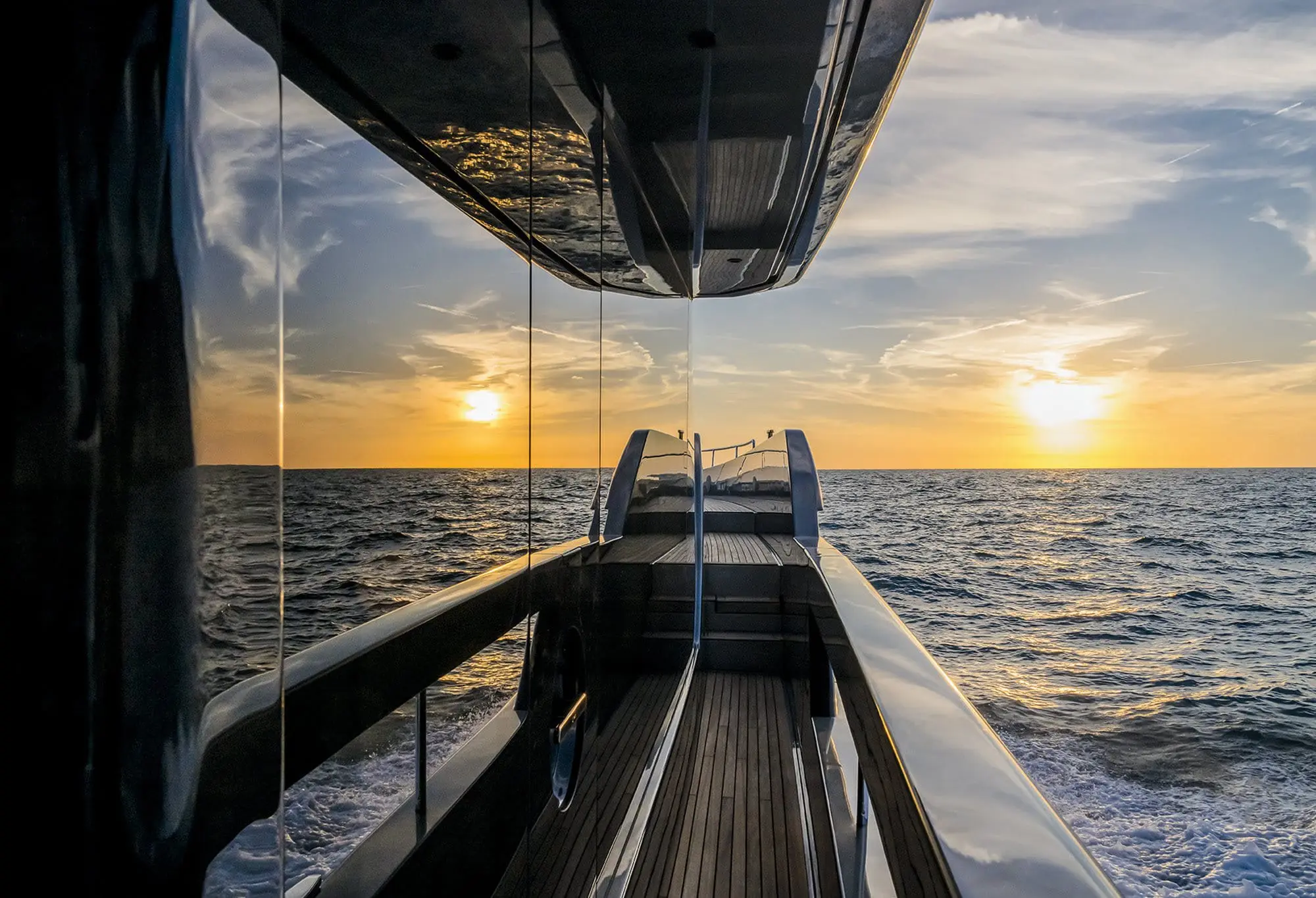 View from the deck of a luxury yacht heading toward the ocean horizon at sunset