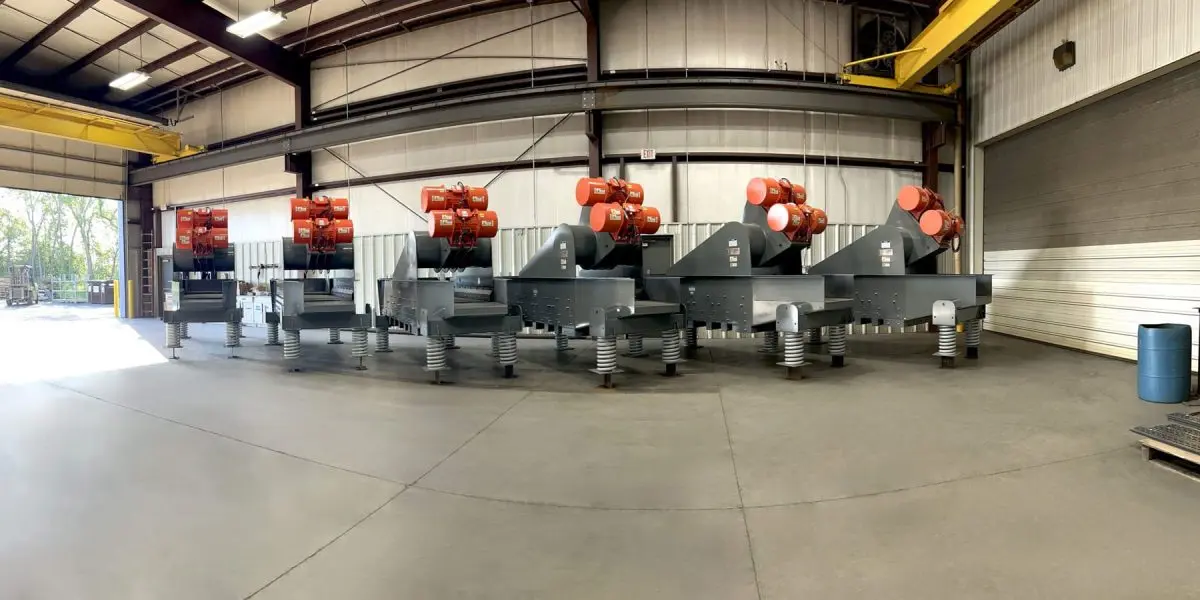 Row of large industrial machines with red motors on spring-loaded bases inside a warehouse.