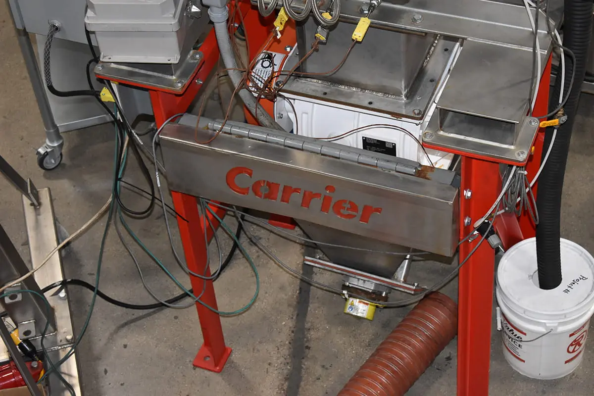 Carrier-branded metal industrial machine on a red frame, with tangled electrical cables and hoses in a workshop setting