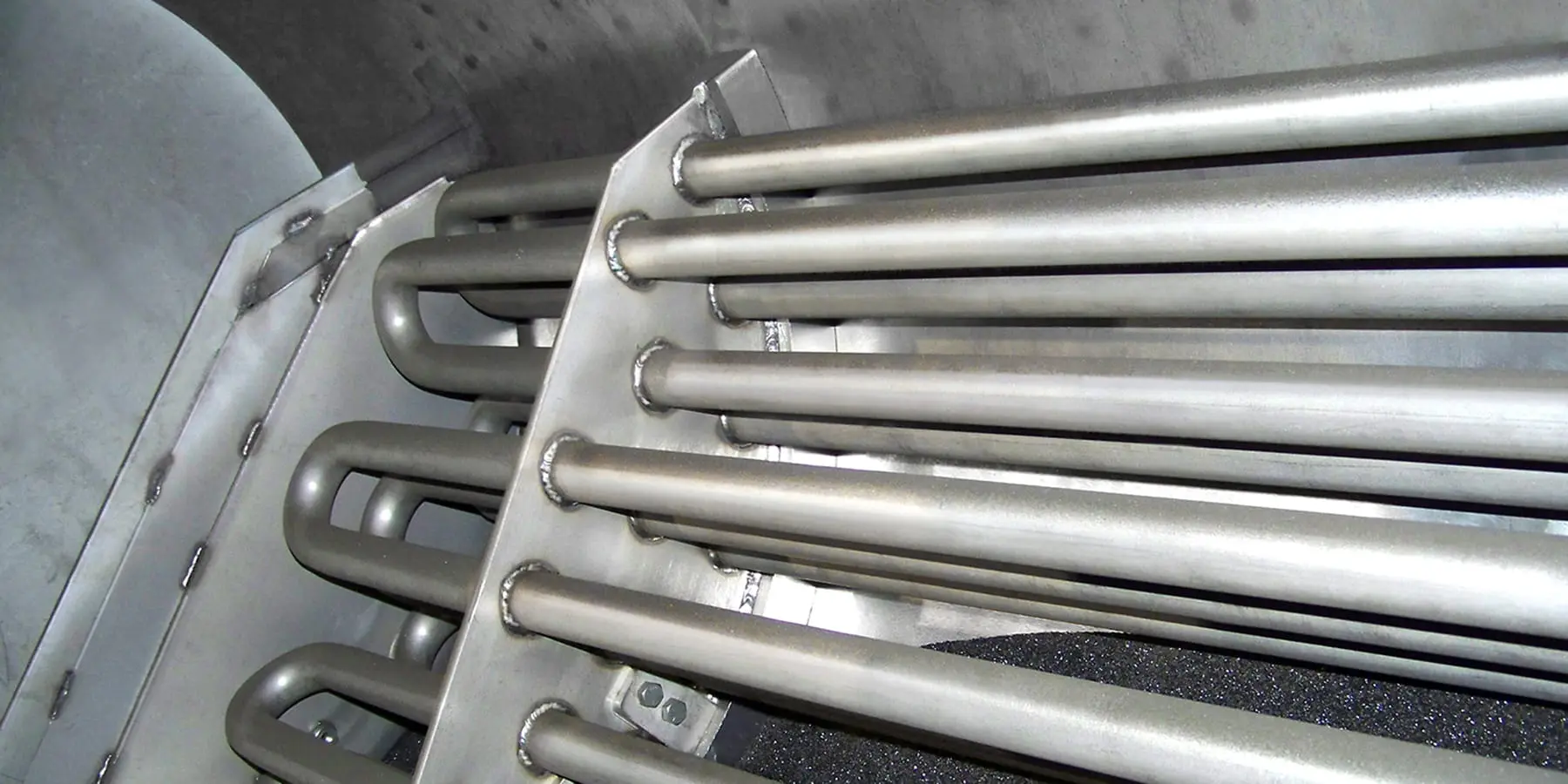 Close-up of parallel metallic tubes welded to a plate inside an industrial enclosure