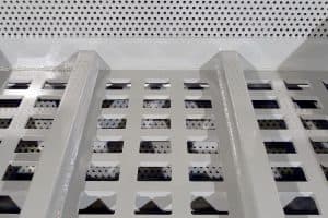 Industrial metal perforated floor/grating with square holes and two supporting beams, viewed from above, in a workshop setting.