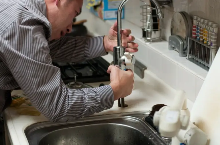 Plumbing Issues in Asheville homes a man repairing a common issue like a leaking kitchen faucet under a sink using tools to fix the fixture.