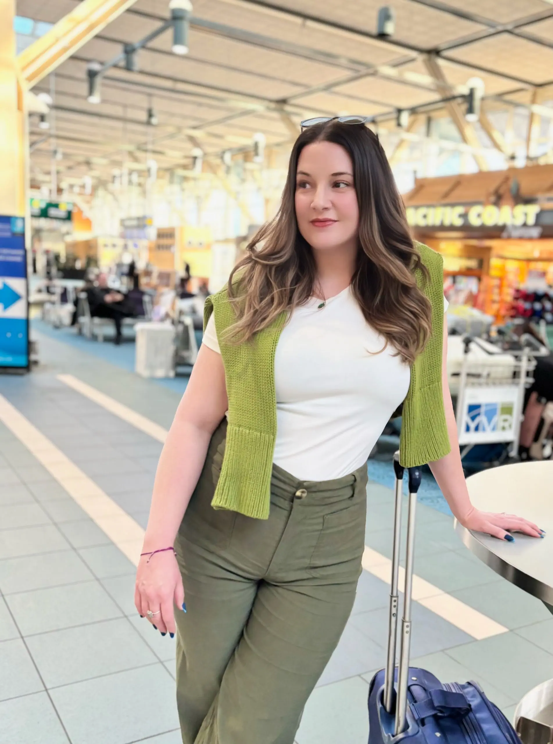 Marybeth Welty at the airport during a layover, standing with carry-on luggage in a bright terminal, looking refreshed and unhurried