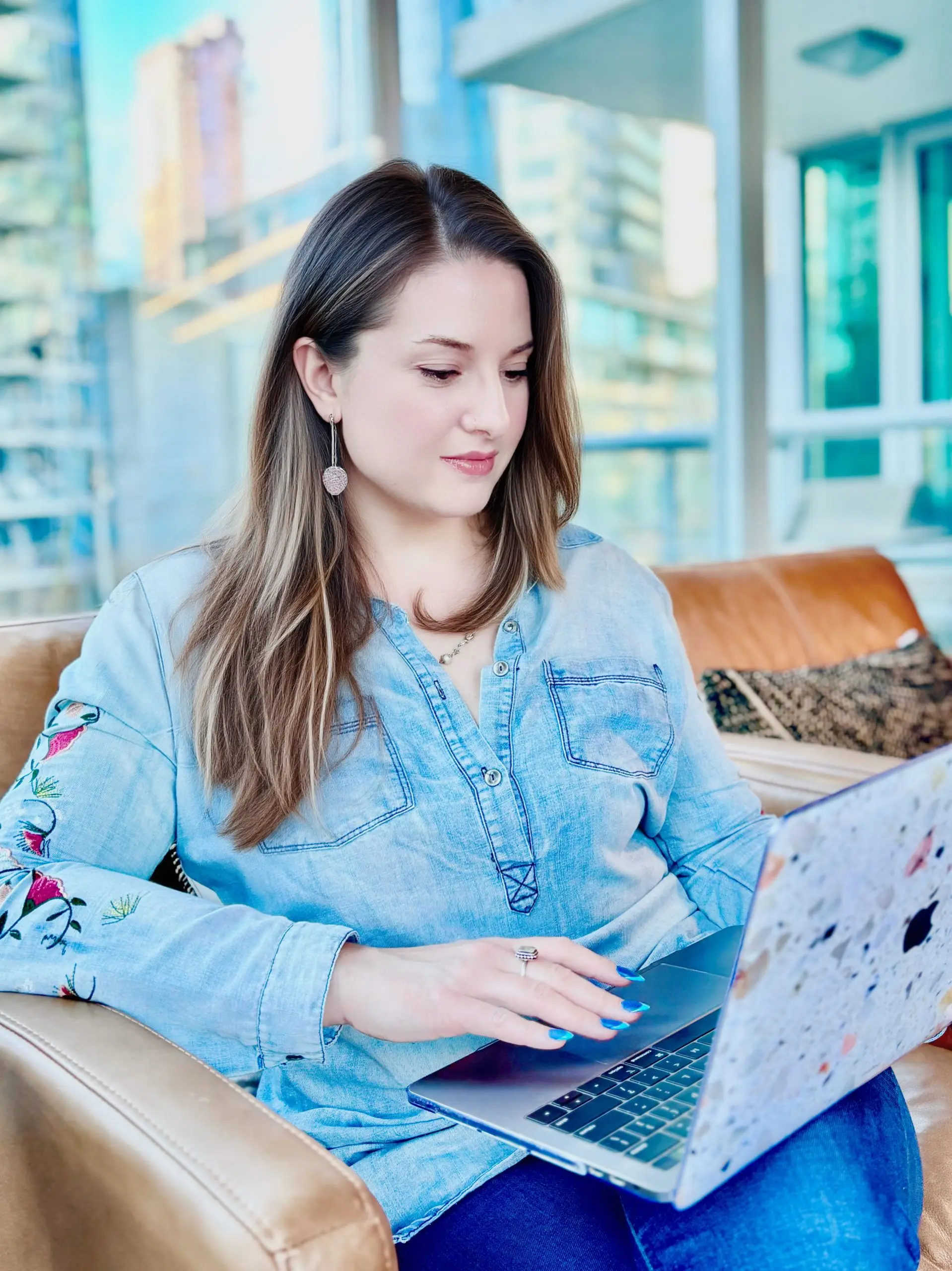 Marybeth Welty working on a laptop by tall windows in a modern Vancouver apartment with city views