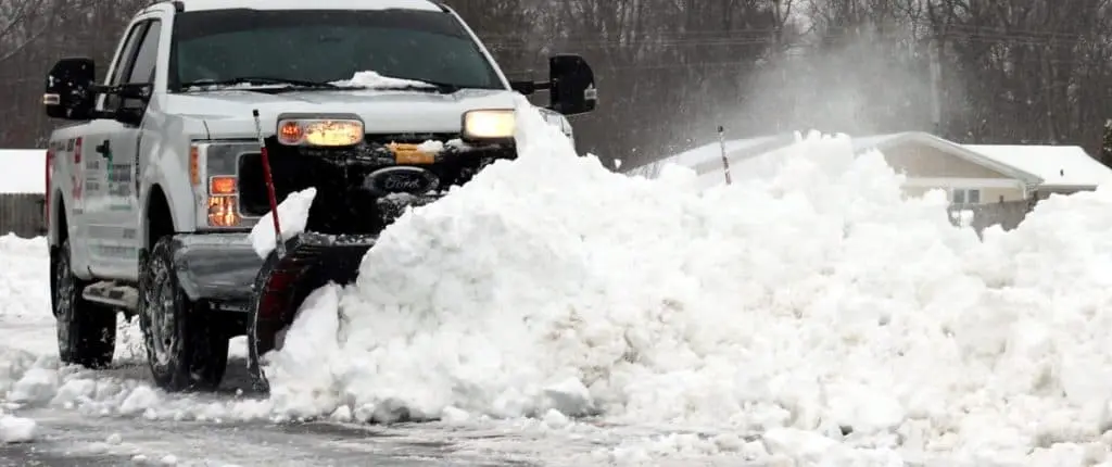 Snow removal service with a truck clearing heavy snow from the road.