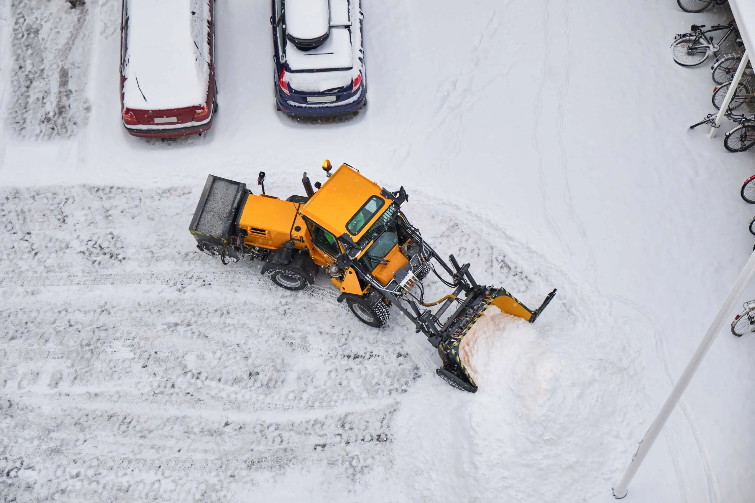 Snow removal with a yellow snow plow on a residential street, clearing snow from the driveway and ro.
