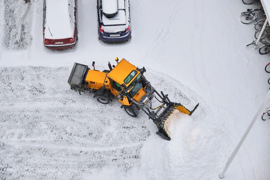 Snow removal with a yellow snow plow on a residential street, clearing snow from the driveway and ro.