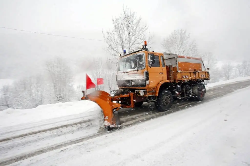 Snow plow clearing snow from a road during winter weather.