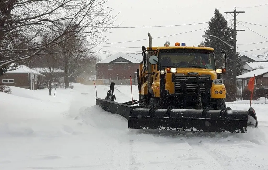 Snow removal with a yellow snowplow truck in a residential neighborhood during winter.
