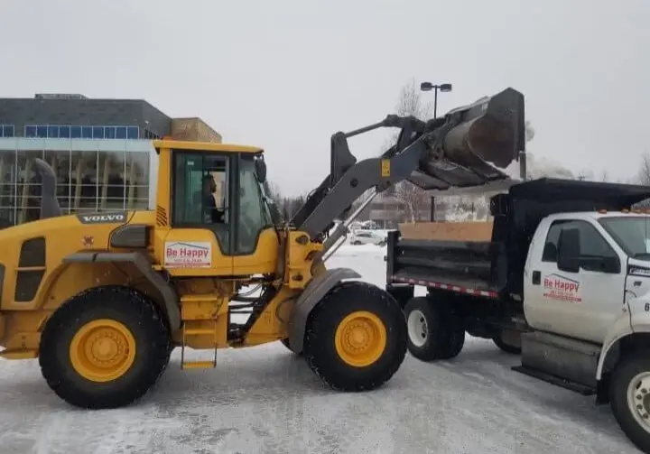 Construction vehicle loading snow into a truck at Be Happy Property Services.