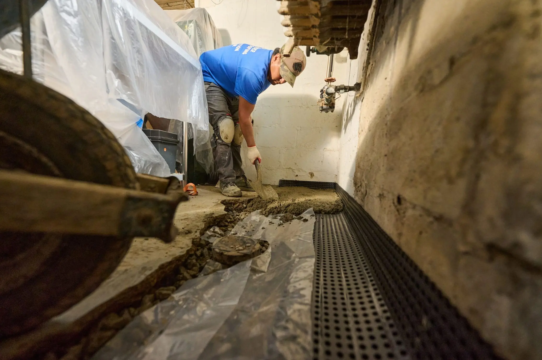 Technician installing an interior drainage system trench in a basement floor for waterproofing and water control.