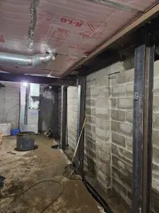 Steel push piers supporting a basement foundation wall and floor joists.