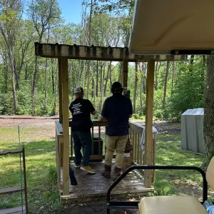 Two men preparing for the Sporting Clay Shoot at Highlands Sporting Clays, surrounded by trees and nature, supporting Highlander Waterproofing's community initiative against human trafficking.