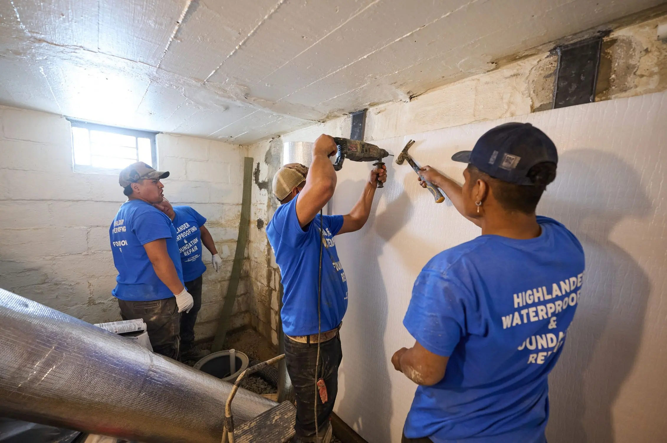 Basement waterproofing professionals installing wall moisture protection system in a residential basement