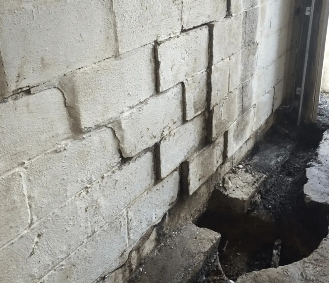 Cracked concrete block wall with visible water damage and exposed foundation, illustrating the need for basement waterproofing and foundation repair.