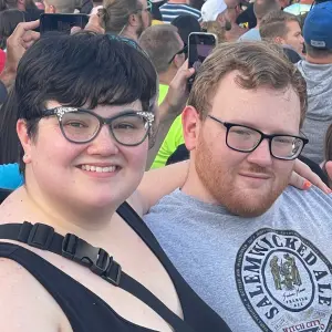 Smiling couple posing together at a vibrant outdoor event, surrounded by a lively crowd, representing community spirit and togetherness at Rock Reggae Relief.