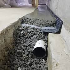 Interior drainage system installation with gravel, perforated pipe, and waterproof membrane for basement waterproofing solutions.
