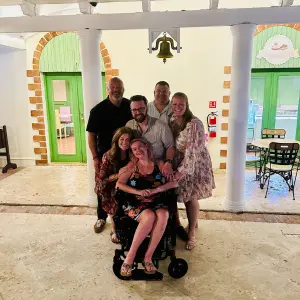 Group of six people posing together in a brightly lit setting, with a woman in a wheelchair at the forefront, symbolizing support and solidarity for ALS awareness.