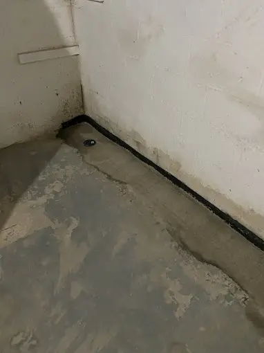 Basement floor with water stains and drainage system illustrating waterproofing needs.