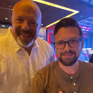 Two men smiling together at a lively event, representing community spirit and connection, likely related to a charitable initiative like Rock Reggae Relief.