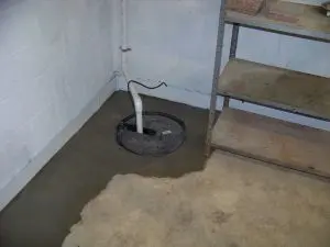 Sump pump installation in a basement corner, with concrete flooring and shelving, illustrating essential waterproofing measures for moisture control.