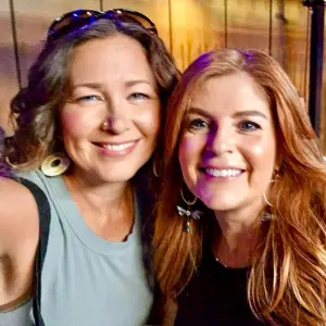 Two smiling women posing together at a vibrant community event, celebrating culture and connection, reflecting the spirit of togetherness emphasized by Highlander Waterproofing's support for local initiatives.