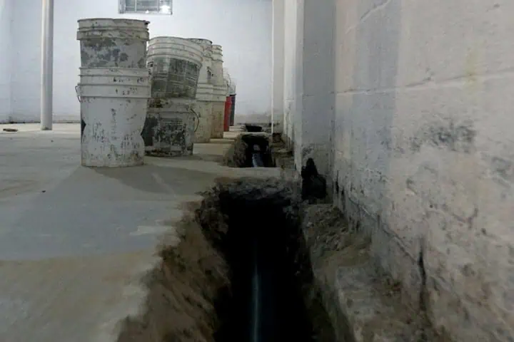 Interior basement waterproofing trench with drainage pipe installation along foundation wall