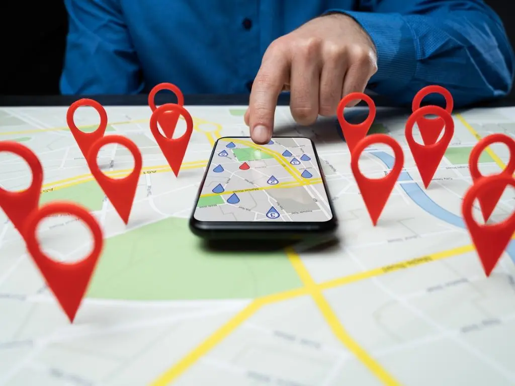 A person using a smartphone with a digital map, surrounded by red location markers.