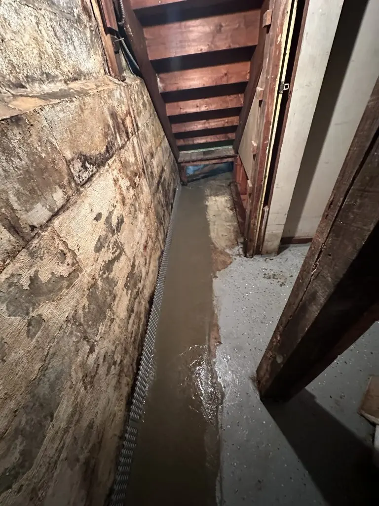 Wet basement wall with water intrusion and interior drainage system installed along foundation