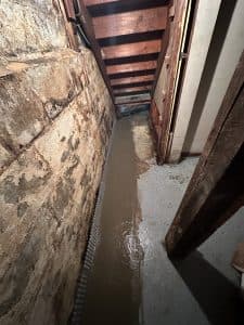 Wet basement wall with water intrusion and interior drainage system installed along foundation