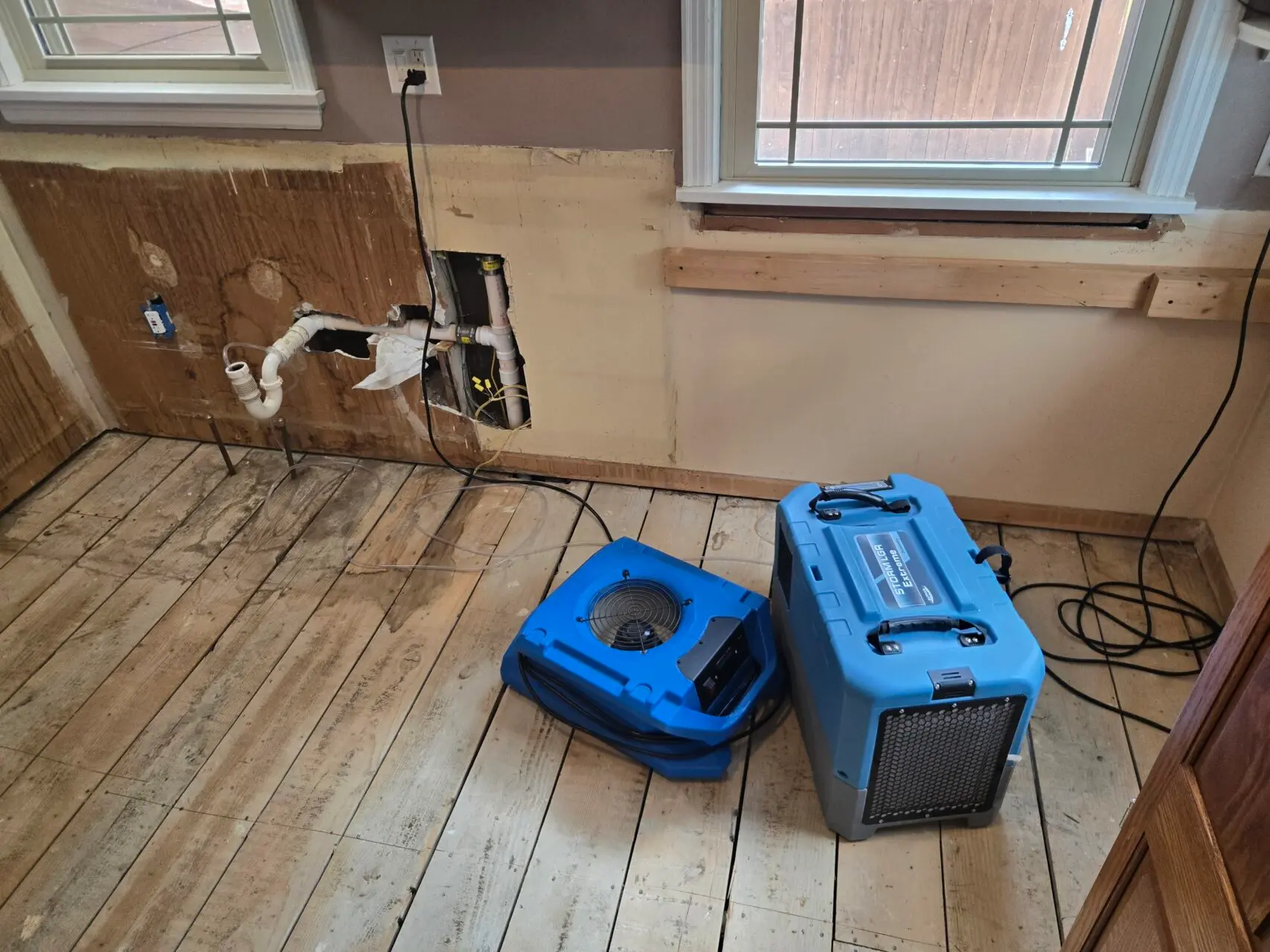 Two blue air movers or drying machines on a wooden floor in a partially stripped room.