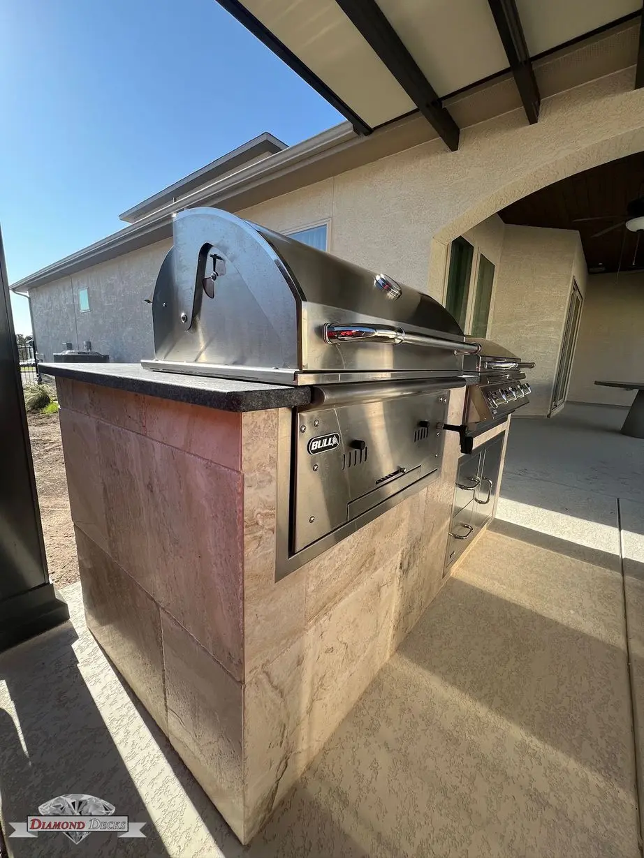 Travertine grill island with Bull grill beside covered patio by Diamond Decks in San Antonio, TX